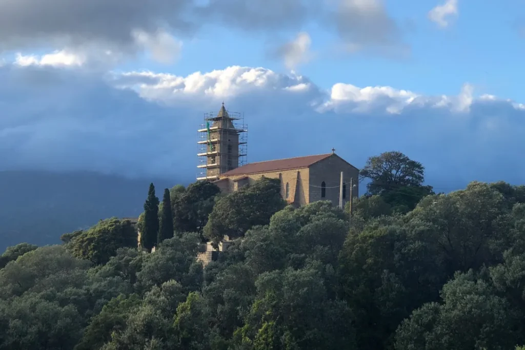 Église en hauteur entourée d’arbres avec un clocher en restauration