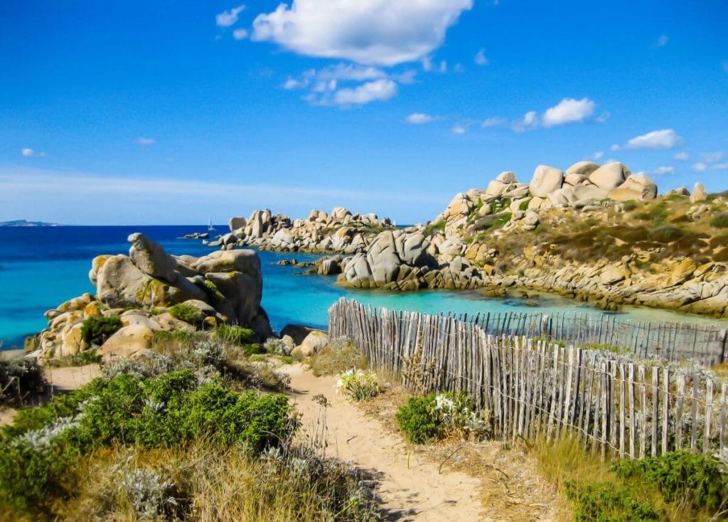 Plage sauvage aux eaux turquoises avec rochers et sentier côtier en Corse