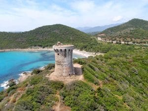 Vue aérienne de la plage de Fautea, avec tour génoise, eau turquoise et végétation, site calme en bord de mer.